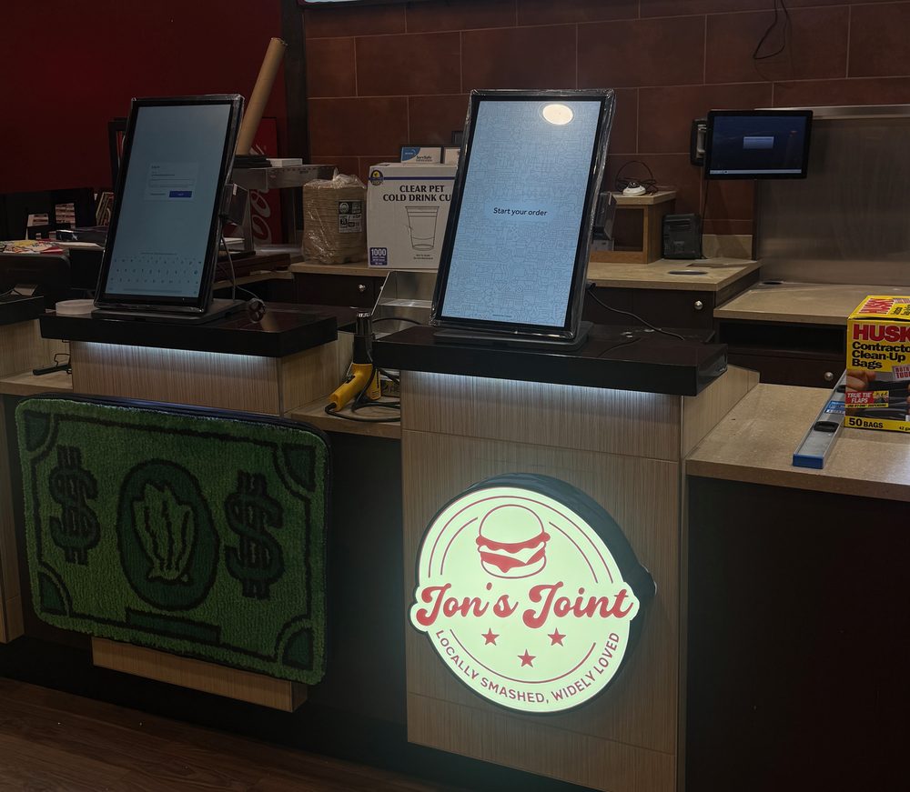 The order counter at Jon's Joint in Sterling, self-order kiosks beneath the lit Jon's Joint sign